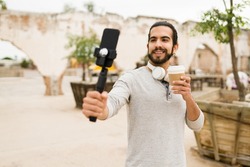 Happy social media influencer filming himself with a smartphone and recording a story or online reel while drinking coffee
