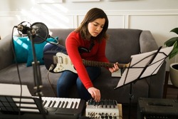 Talented young woman using a sound mixer while writing a new song on the electric guitar at home