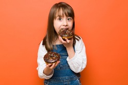 Pretty Caucasian little girl eating so much sweet food and about to get some sugar rush from so many donuts