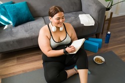 Successful diet. Happy obese woman smiling and feeling happy while using a journal to track her fitness journey and diet