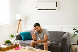 Upset man sweating during a heat wave in the summer while at home with a cold ac unit