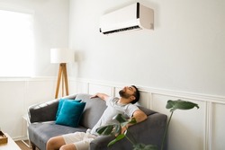 Relaxed man chilling and resting on the sofa while enjoying the new ac unit during a hot summer