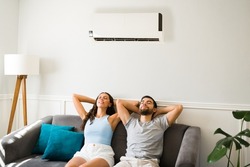 Latin attractive couple relaxing and resting on the couch with the air conditioner on during a hot summer 