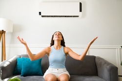 Happy latin woman enjoying the cold air flow of her air conditioner during a hot summer at home 