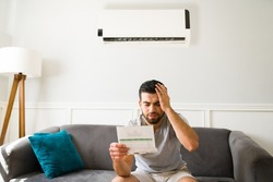 Expensive bills. Stressed latin man looking at the high electricity bill because of the air conditioning