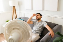 Relaxed man cooling with a cold lemonade and turning on the electric fan during a heat wave