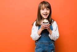 Portrait of a beautiful kid dressed casual and holding a delicious chocolate cupcake in her hands and smiling