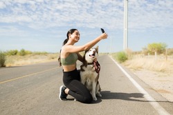 Gorgeous latin woman smiling while taking a selfie with his husky dog while exercising outdoors