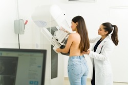 Rear view of an hispanic young woman getting a mammogram to check for breast cancer with the help of a female doctor at the imaging diagnostic center