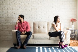 Husband and wife sitting on the couch and not talking after an argument at home. Social Distancing concept