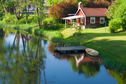Old red wooden house in the village Hoegsby, Sweden,in the foreground the river Eman.