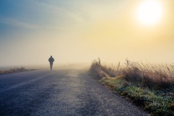 A person walk into the misty foggy road in a dramatic mystic sunrise scene with abstract colors