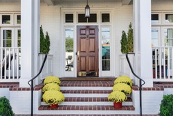 flowering yellow pots and green plants line the entryway of a custom home that features a front door that is brown