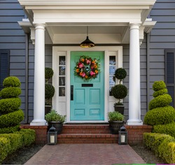 Beautifully decorated turquoise colored front door of traditional home. Brick path and trimmed hedges.