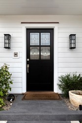 Front door, black front door with a white wall, light fixtures and potted plants