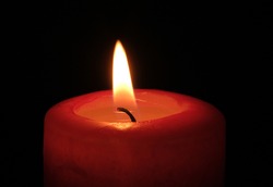 Red paraffin mournful commemorative thick candle burns on a black background close-up