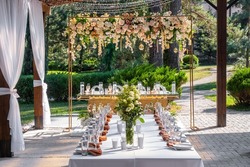 Wedding table setting decorated with fresh flowers. Wedding floristry. Banquet table for guests outdoors with a view of green nature at sunset. Bouquet with roses. 