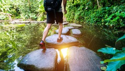 Male hiker with backpack crossing a river on stones.