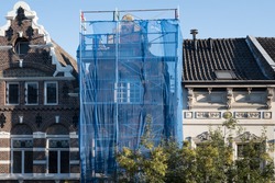 Scaffolding with protective net against historic building to prevent paint and building material from falling on the street and people, during renovation in a street in Maastricht, the Netherlands