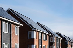 Solar panels mounted on the tile roofs of a row modern new-build houses in a street in Lemmer, Friesland, the Netherlands with sun and blue sky. Sustainable energy