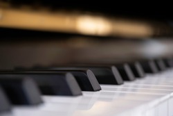 Close side view of shiny black and white piano keys with the reflection of the golden brass edge from low angle with shallow depth of field. Focus on the fourth black key from the center left