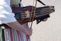 Woman in Swedish traditional costume plays folk music on a Swedish nyckelharpa in a close-up with focus on the bow, strings and bridge