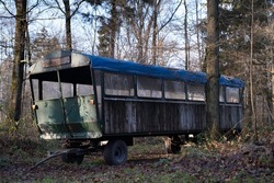 Worn and rusted long metal covered wagon with wooden sides parked among the trees in an autumn forest