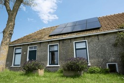 Older renovated small rural house in a green environment with solar panels on the roof in the village of Warns in the Netherlands. Old-fashioned and modern at the same time. Sustainable energy