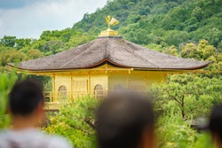 Long shot of top of golden pavilion with blurred tourist heads