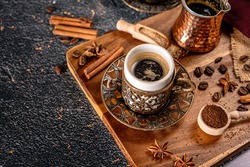 Cup of turkish coffee on black background with spices, coffee beans and sand coffee pot
