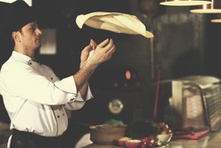 Skilled chef preparing dough for pizza rolling with hands and throwing up