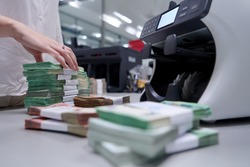 Bank employees using money counting machine while sorting and counting paper banknotes inside bank vault. Large amounts of money in the bank