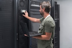 Data Center Engineer Using Laptop Computer Server Room Specialist Facility with Male System Administrator Working with Data Protection Network for Cyber Security or Cryptocurrency Mining Farm.
