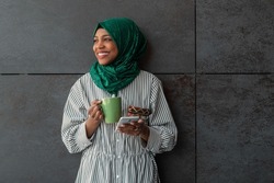 African Muslim businesswoman with green hijab using mobile phone during coffee break from work outside