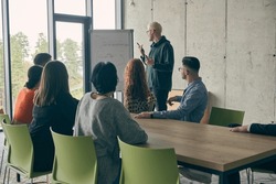 In a modern office setting, a group of business professionals attentively listens to a captivating presentation delivered by their young colleagues, showcasing their teamwork, engagement, and
