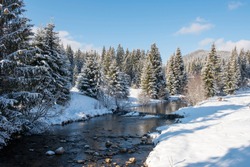 Winter water stream in the forest with snow covered trees 