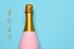 New Years 2023 Concept. A Pink Champagne bottle on a blue teal background, with the text 2023 on one side.