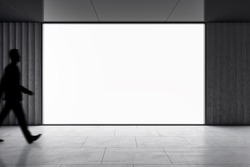 Dark man silhouette walking by big blank white screen with space for your logo or text in abstract empty hall area with dark ceiling and floor, mockup