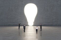 Creative idea and brainstorm concept with pensive men and women in the center of empty hall with glowing hole in the form of light bulb in grey wall