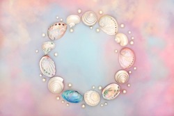 Sea shell wreath with oyster pearls on rainbow coloured cloud and sky background. Ethereal heavenly nature concept for birthday, birth of child, anniversary or holiday greetings card. Top view.