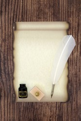 Old fashioned parchment scroll with white feather quill pen, ink bottle and blotter. For manuscript, diploma, document and letter composition.  On rustic wood background, top view, copy space.
