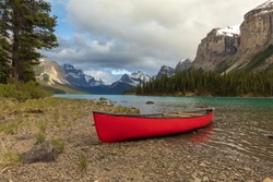 Empty red canoe on a rocky shoreline of a pristine alpine lake surrounded by mountains