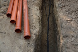 Safety supply to house new insulated internet, gas cord, red metal-plastic tap system construction lay in pit dug in garden. Top view with space for text on grey clay earth. Telecom service industry
