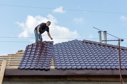 Workers install metal roofing on the wooden roof of a house. Technology