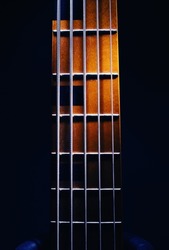 Closeup view of neck of five strings bass guitar, highlighted shapes.
