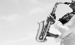 Saxophonist playing on saxophone on blue sky background 