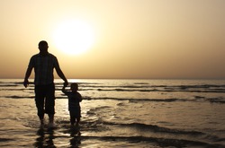 Silhouette image of father and his child by the sea shore, sunset