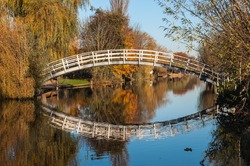 Wooden footbridge reflected in the mirror smooth water surface of a small canal in the Netherlands.