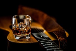 An acoustic guitar lays on it's back while a glass of whiskey with ice rests on it's top