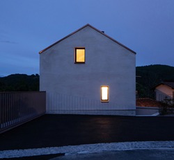 Single-family house facade in Switzerland, evening and almost night situation with two yellow illuminated windows. Romantic and silent photo. A fairy tale